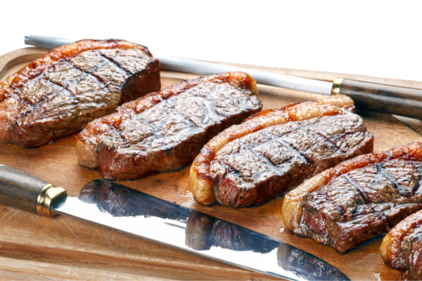 Carne para churrasco: melhores cortes, preparo e organização 5 Cortes de carne para churrasco grelhados, prontos para servir, sobre tábua de madeira.