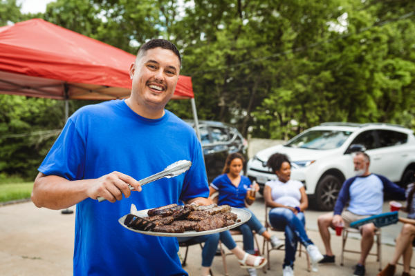 Churrasco de Dia dos Pais: melhores carnes, bebidas e dicas de organização 5 Homem sorridente preparando churrasco com carne na grelha ao ar livre durante reunião familiar.
