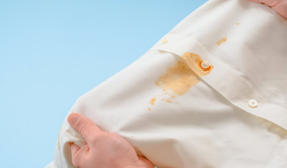 Como tirar mancha de roupa: aprenda a remover marcas difíceis 1 Camisa branca com mancha de molho sendo segurada por uma pessoa, ilustrando técnicas e produtos para tirar manchas de roupa de forma eficiente.